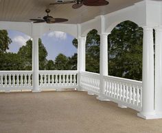 an empty porch with white pillars and ceiling fans on the roof, along with trees in the background