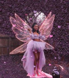 a woman dressed as a fairy standing in front of purple flowers with petals all over her body