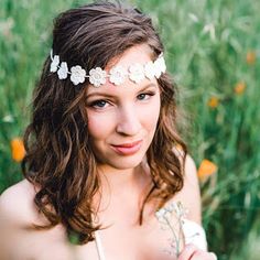 a woman wearing a white flower headband in the middle of some grass and flowers