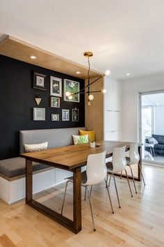 a dining room table with white chairs next to a bench and pictures on the wall