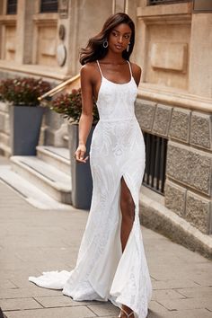 a woman in a white dress is walking down the street with her leg slit open