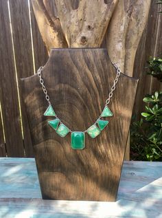 a necklace with green glass beads and silver chains on a wooden stand next to a tree