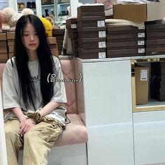 a woman sitting on top of a pink chair next to boxes in a room filled with furniture