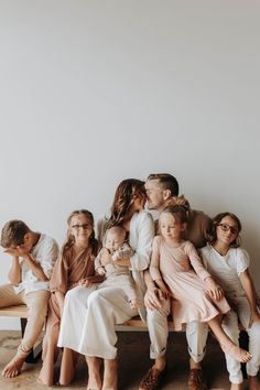 a group of people sitting next to each other on top of a wooden bench in front of a white wall