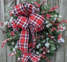 a wreath with red and white plaid ribbon hanging on a fence