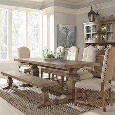 a dining room table with chairs and a bench in front of the window on a rug