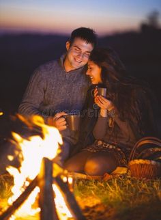 a man and woman sitting next to a campfire at night drinking coffee royalty photo