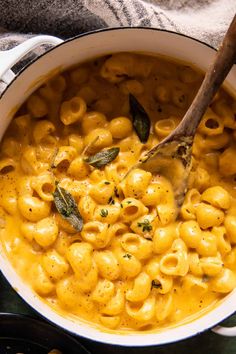 a pot filled with macaroni and cheese on top of a table next to a wooden spoon