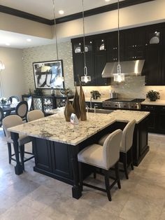 a large kitchen with black cabinets and marble counter tops, along with white chairs in front of the island