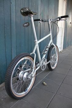 a white bicycle parked next to a blue building on a sidewalk with no one around it