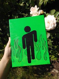 a hand holding up a green sign with a man on it in front of some flowers