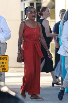 a woman in a red dress is walking down the street with other people behind her