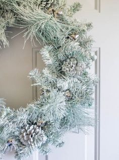 a wreath with pine cones and ornaments hanging on the front door