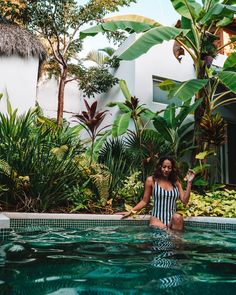 a woman sitting on the edge of a pool surrounded by tropical plants and greenery