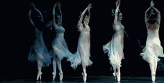 four ballet dancers in white dresses are performing on stage with their arms up and legs spread out