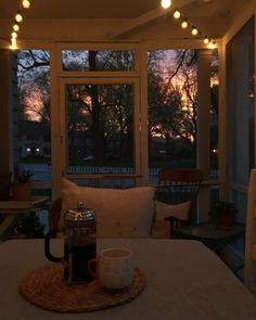 a coffee cup sitting on top of a table next to a window with the sun setting