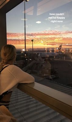 a woman is looking out the window at an airport with a sunset in the background