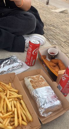 a person sitting on the ground with some food and sodas in front of them