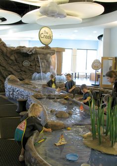 children are playing in an indoor water play area with fake rocks and reedy plants