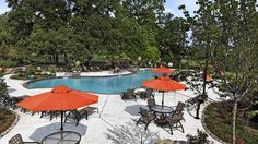 an outdoor patio with tables and umbrellas next to a swimming pool surrounded by trees