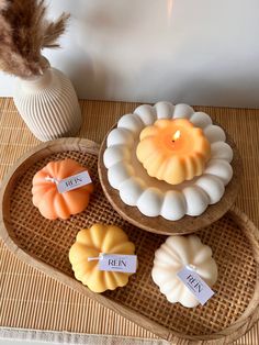 three pumpkin candles sitting on top of a wooden tray next to a vase with a feather