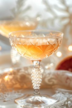 two glasses filled with liquid sitting on top of a white table covered in christmas lights