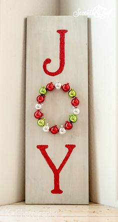 a wooden sign with the word joy spelled in red and green beads hanging on it's side