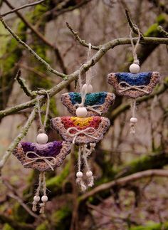 three crocheted hearts hanging from a tree branch in the woods with beads and balls attached to them