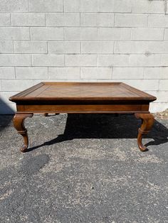 an old wooden coffee table sitting in front of a white brick wall on the sidewalk