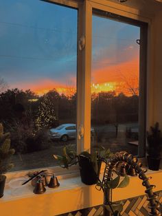 the sun is setting in the distance through two large windows with plants on each window sill