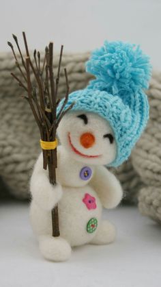 a small white snowman with a blue knitted hat holding a twig in his hand