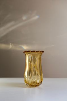 a yellow glass vase sitting on top of a white table next to a gray wall