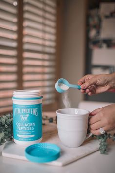 two hands sprinkling sugar into a bowl with a blue plastic spoon on a white table