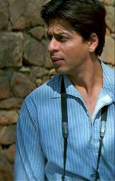 a man wearing suspenders and a blue shirt is standing in front of a stone wall