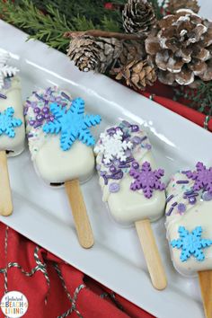 four snowflake covered popsicles on a white platter with pine cones in the background