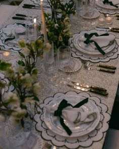 the table is set with black and white plates, silverware, candles and flowers