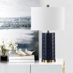 a blue lamp sitting on top of a table next to a white vase filled with flowers