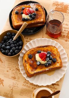 two pieces of french toast with berries and blueberries on top next to a bowl of syrup