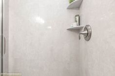 a bathroom with a shower head, shelf and toilet paper dispenser on the wall