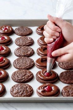 someone is decorating chocolate cookies with cranberry icing on a baking sheet