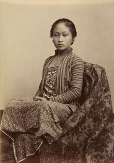 an old black and white photo of a young woman sitting on a chair with a blanket over her head