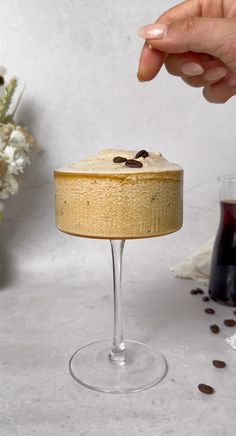 a person reaching for a piece of cake on top of a wine glass with coffee beans scattered around it