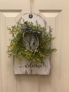 a welcome sign hanging on a door with a wreath and ribbon attached to the front