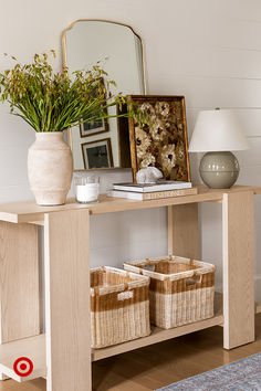 a wooden table topped with baskets filled with flowers next to a mirror and lamp on top of a hard wood floor