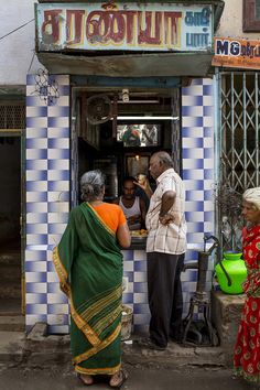 three people standing in front of a store with blue and white checkered tiles on the wall