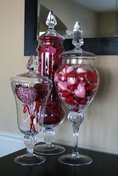 two glass vases with candy in them sitting on a table next to a mirror