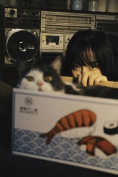 a woman is looking out from behind a box with a cat in front of her