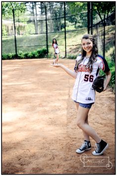 a young woman holding a baseball glove and ball in one hand while standing on a dirt field