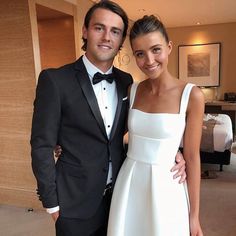 a man in a tuxedo standing next to a woman in a white dress