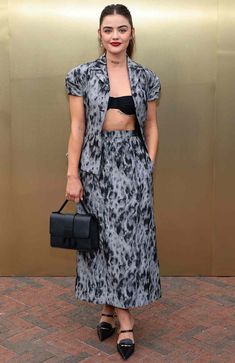 a woman standing in front of a gold wall wearing a black and white dress with an animal print